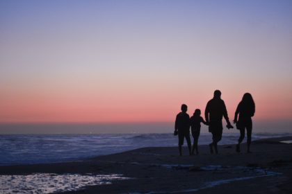 silhouette of 3 men and woman standing on beach during sunset